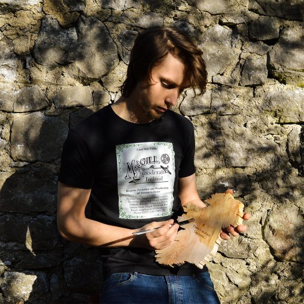 Furniture Designer-Maker Cian Magill applying oil to a wooden map of Ireland, stone wall in background.