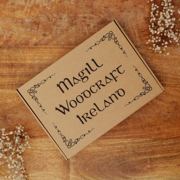 Top view of a Celtic leaf corner Magill Woodcraft Ireland cardboard gift box for a wooden map of Ireland wall art piece, as it sits on top of a brown wooden table with slowers in each corner.