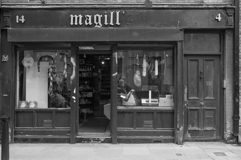 Magill's Delicatessen shop front in Dublin, Ireland. Image is in black and white and meats are hanging in the window