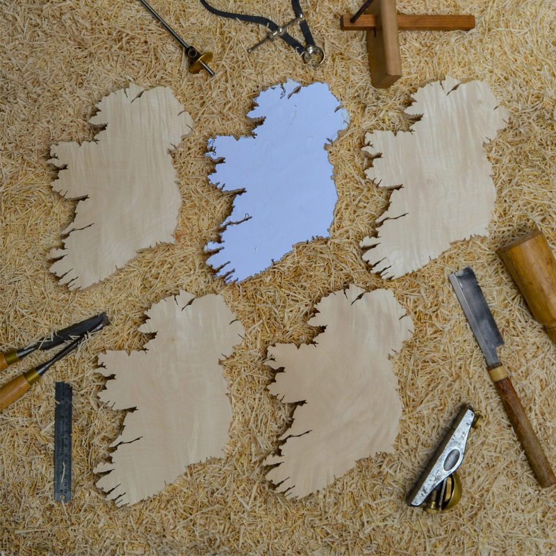 Top view of some Irish wooden gifts wall maps on top of a woodorking bench with woodworking tools around such as chisels, a block plane, and a marking guage