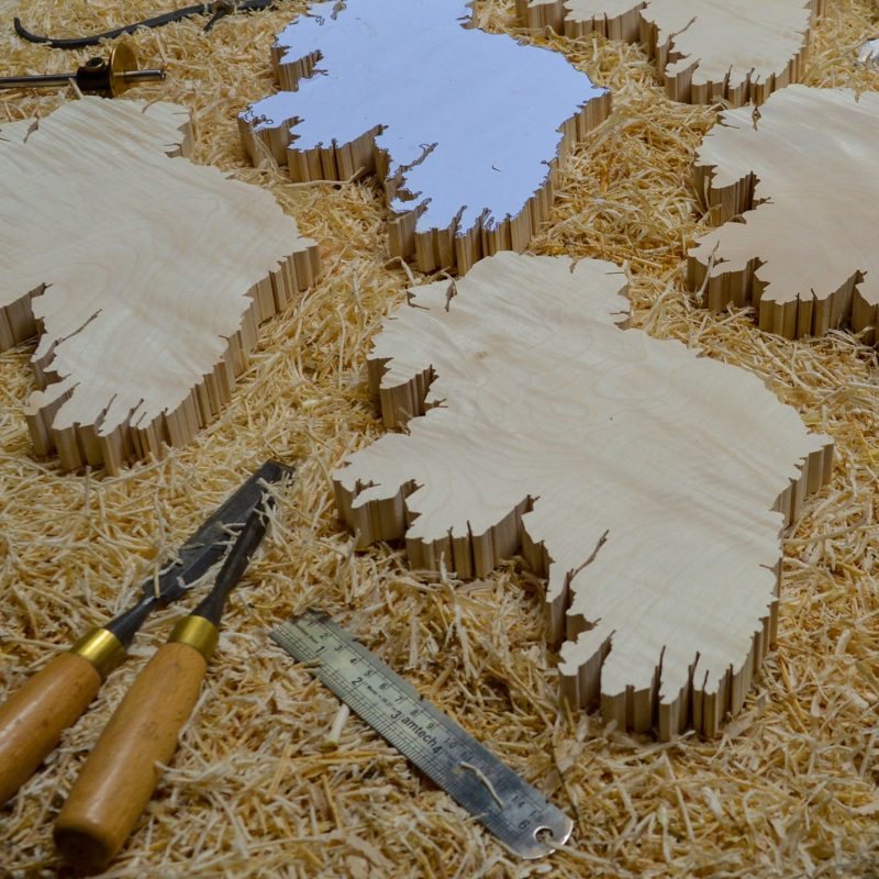 5 Wood maps of Ireland wall art to be made into Irish wooden gifts, on top of a woodorking bench with woodworking tools around such as chisels, a block plane, and a marking guage 