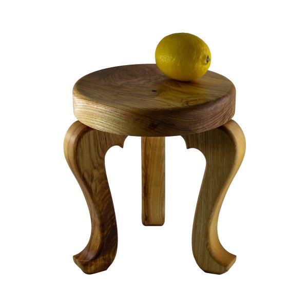 Handmade 3 legged wooden stool made from native Irish Ash wood on a white background. There is a yellow lemon on top of the wood stool for scale. The seat is round and woodturned. The legs are in the Queen Ann style. The stool is about 12" tall x 10" in diameter.