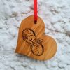 Wooden love heart decoration engraved with Gaelic word for "Love" - "Grá". With red ribbon hanging on a white wall.