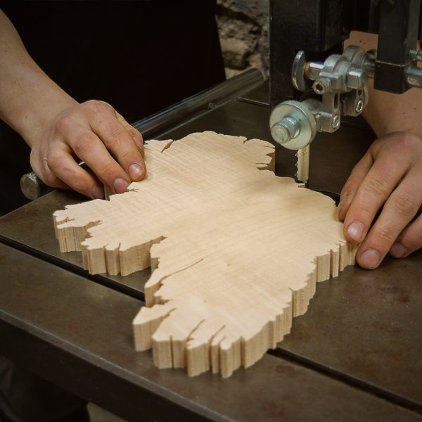 Close up of Furniture Designer-Maker Cian Magill's hands on a Wooden Map of Ireland Wall Art piece. He is carving the Ireland map using a bandsaw which shows its blade and cast-iron table.