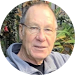 Smiling man with glasses headshot wearing a grey hoodie/ sweatshirt with green plants in background