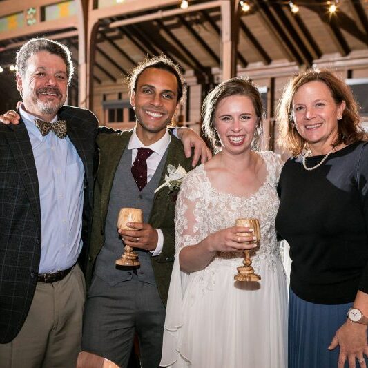 Bride and groom holding wooden goblets at wedding with barn interior in the background.